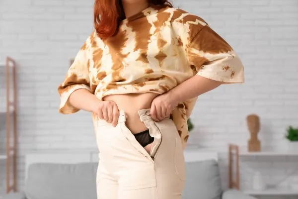 Image of woman trying to do her trousers up after pregnancy weight gain Ayr