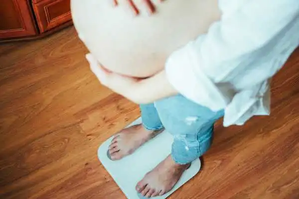 Image of woman weighing herself and experiencing weight gain through pregnancy Ayr